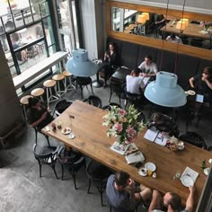 people sitting at tables in a restaurant with large windows looking out on the city street