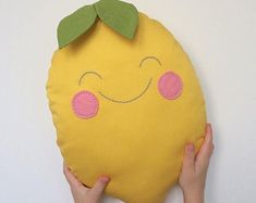 someone is holding up a pillow made to look like a lemon with a green leaf on it