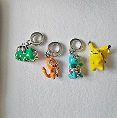 four different colored charms sitting next to each other on a white surface with one charm in the shape of an elephant