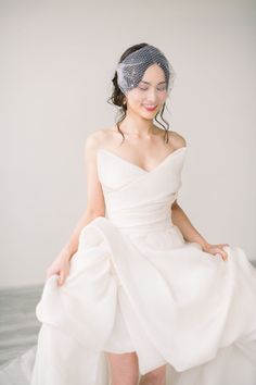 a woman in a white dress and veil sitting on a bed with her legs crossed