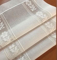 three pieces of white fabric with lace on them sitting on top of a wooden table