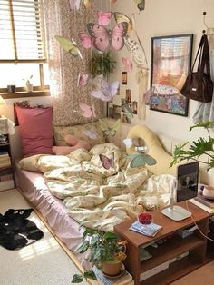 a bed with lots of pillows on top of it next to a table and potted plants