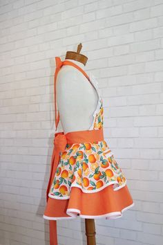 an orange apron dress on a mannequin with a white brick wall behind it