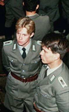 two men in uniform standing next to each other and looking at the same person's face