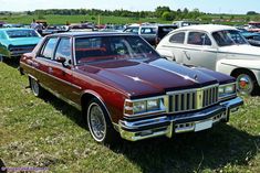 an old car parked in a field with other cars behind it and people standing around