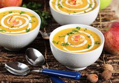 three white bowls filled with carrot soup and garnished with parsley on top