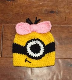 a crocheted hat with a pink bow and eyeballs on it sitting on top of a wooden floor