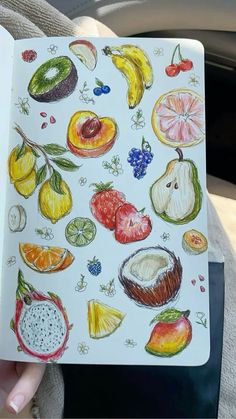 a person holding up a notebook with fruit drawings on it