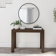 a mirror on the wall above a wooden table with books and plants in front of it