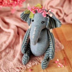 an elephant stuffed animal with flowers on its head sitting on a pink blanket and wooden floor