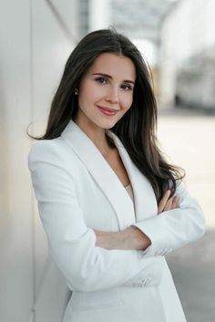 a woman in a white suit is posing for a photo with her arms crossed and smiling at the camera