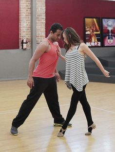 a man and woman dancing on a wooden floor in an indoor dance studio with red walls