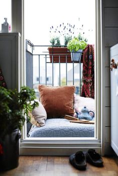 an open door leading to a balcony with potted plants and shoes on the floor