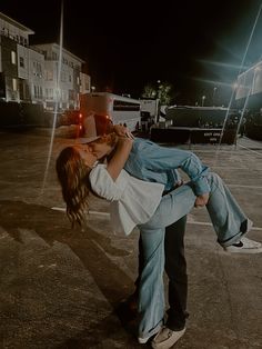 a man and woman kissing in an empty parking lot at night with the lights on