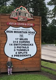 a young child standing in front of a sign for iron mountain road, with information about the area