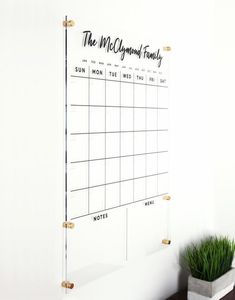 a dry erase calendar hanging on a wall next to a potted plant