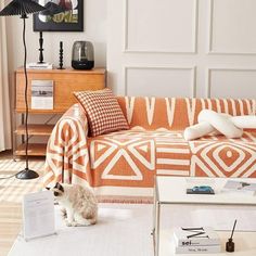 a cat sitting on the floor in front of an orange and white couch with pillows