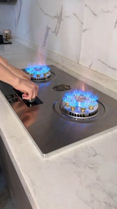 a woman is touching the burners on a stove top that has blue flames in it