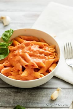 a white bowl filled with pasta and sauce on top of a wooden table next to garlic