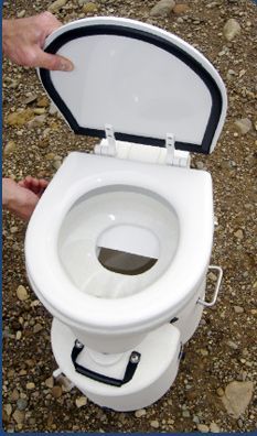 a white toilet sitting on top of a rocky ground next to a person's hand