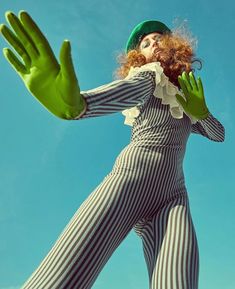 a woman dressed in striped clothing and green gloves with her hands out to the side