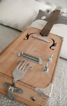 a wooden guitar case sitting on top of a bed next to pillows and pillow cases