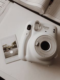 a white camera sitting on top of a table next to an open book