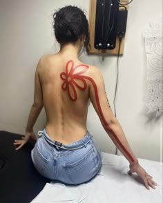 a woman sitting on top of a bed with her back turned to the camera and tattooing