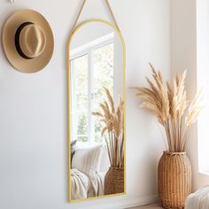 a large mirror hanging on the wall next to a vase with dried grass in it