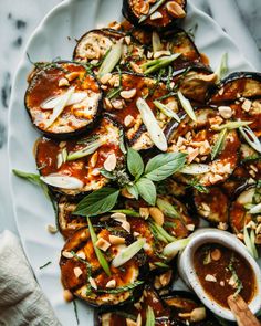 grilled eggplant with sauce and herbs on a white plate next to a napkin