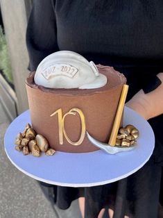 a woman holding a chocolate cake with the number ten on it and gold decorations in front of her