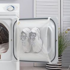 pair of white tennis shoes sitting on top of a dryer in front of a washing machine