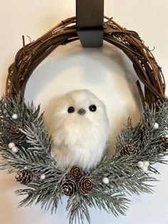 a white owl sitting in a wreath with pine cones