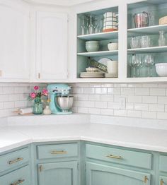 a kitchen with green cabinets and white marble counter tops in the center, along with dishes on shelves