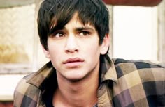 black and white photo of young man with plaid shirt looking at the camera while standing in front of an open window