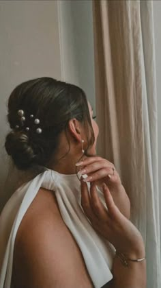 a woman is looking out the window with her hands on her face and wearing pearls in her hair