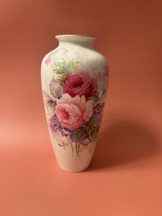 a white vase with pink and purple flowers painted on the side, against a peach background