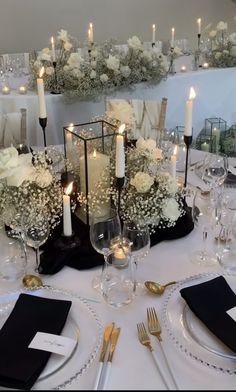 the table is set with silverware and white flowers in vases, candles, and napkins