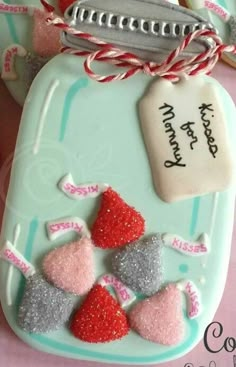 decorated cookies are sitting on a table next to pink and silver candies with tags