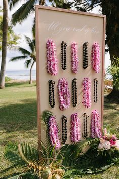 a sign that has flowers on it in front of some grass and palm trees with the ocean in the background