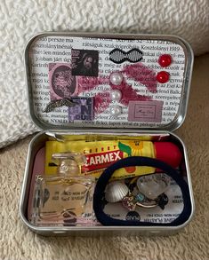 an open tin box with various items inside on a white carpeted floor next to a pillow