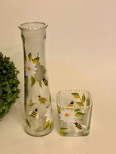 a glass vase with flowers and bees on it next to a small square dish holder