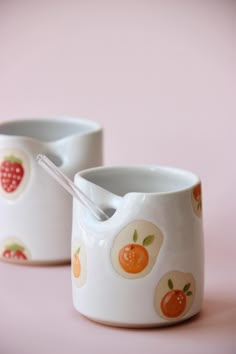 two white cups with oranges and strawberries on them, one has a spoon in it