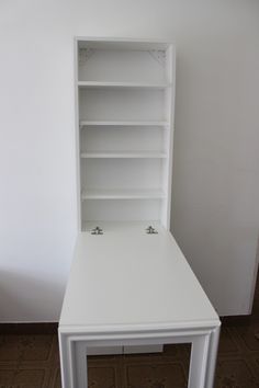 a white desk with shelves on the top and bottom shelf in front of it, against a white wall