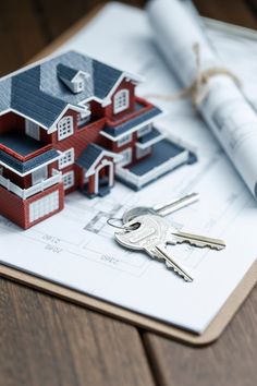 a house model on top of blueprints with keys in the foreground and rolled up construction plans behind it