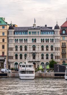 a large white boat floating on top of a river next to tall buildings with green roofs