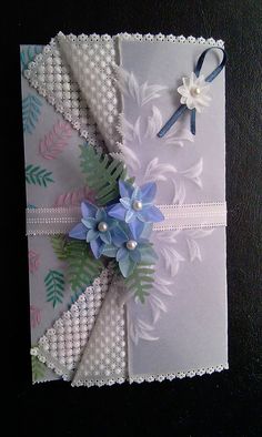 a white card with blue flowers and pearls on the front, tied in a ribbon