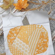 an orange and white patchwork piece on top of some leaves