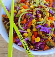 a white bowl filled with assorted veggies next to two green chopsticks