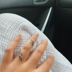 a woman's hand with a tattoo on her left thumb and fingers, sitting in the passenger seat of a car